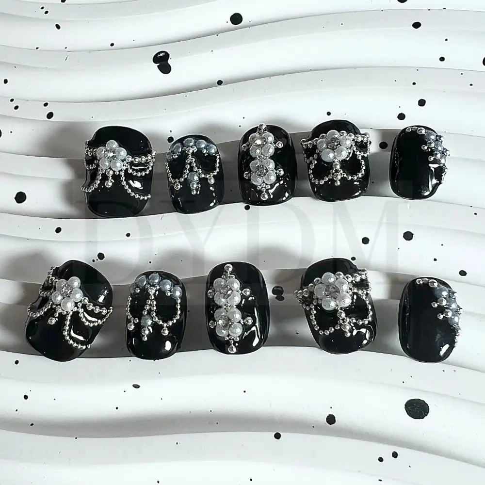 Enchanting Noir handmade press on nails, featuring captivating black nails adorned with delicate pearl petals forming a blossoming flower. A sparkling crystal at the center adds allure, creating an elegant and enchanting manicure