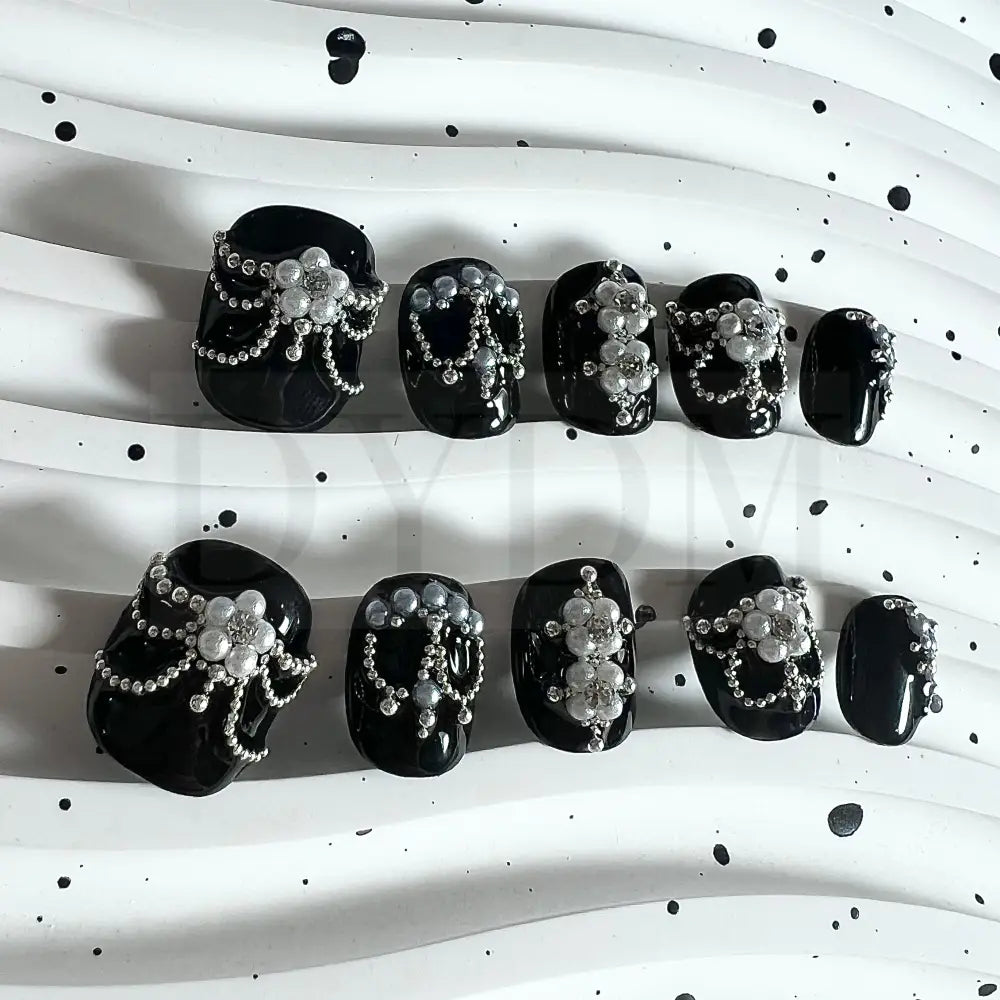 Enchanting Noir handmade press on nails, featuring captivating black nails adorned with delicate pearl petals forming a blossoming flower. A sparkling crystal at the center adds allure, creating an elegant and enchanting manicure