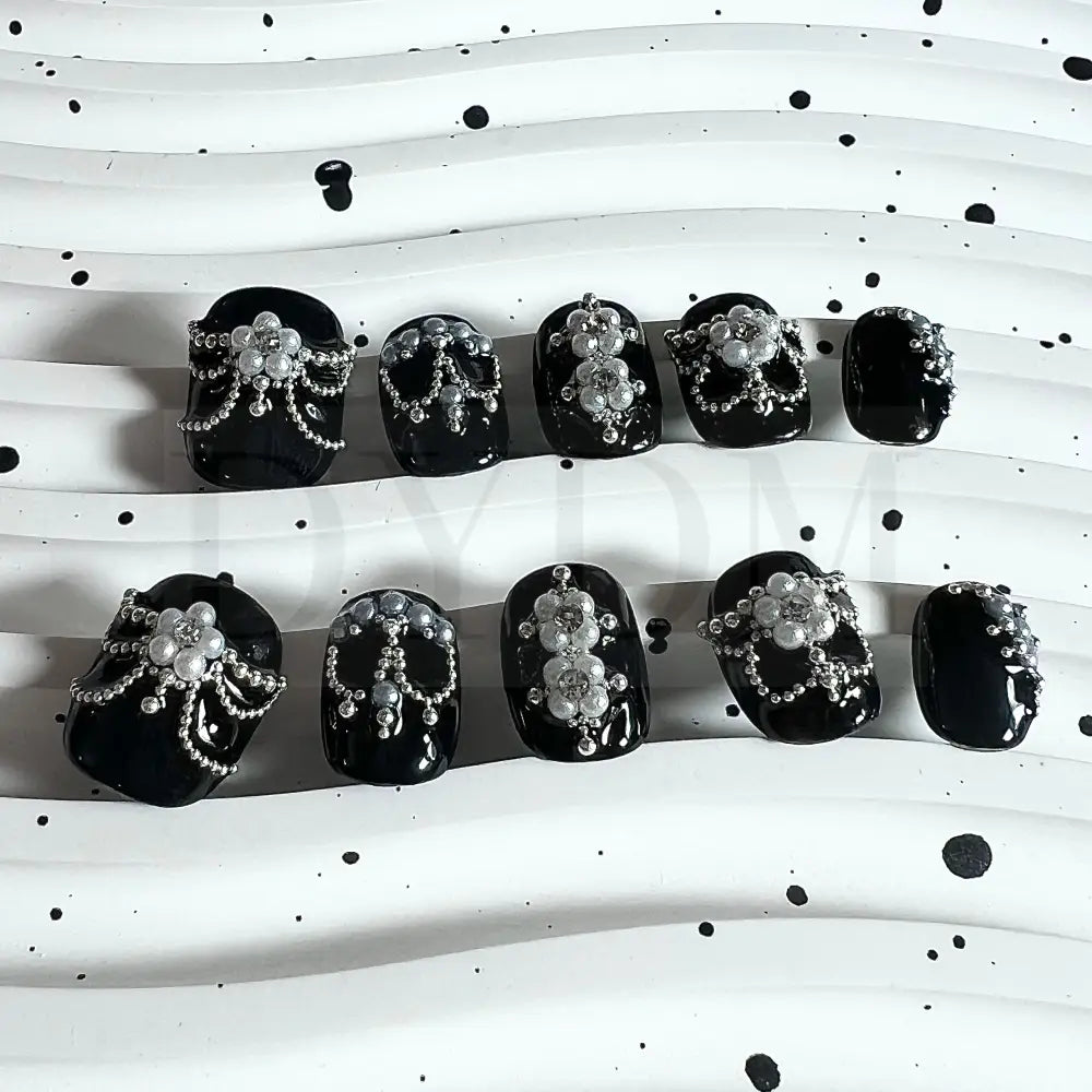 Enchanting Noir handmade press on nails, featuring captivating black nails adorned with delicate pearl petals forming a blossoming flower. A sparkling crystal at the center adds allure, creating an elegant and enchanting manicure