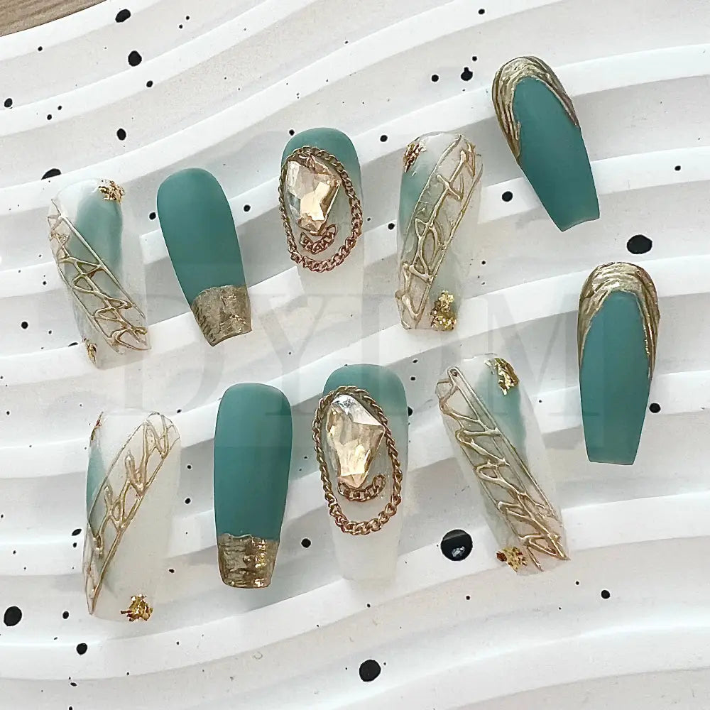 French Rococo Featuring an aqua base, these handmade press-on nails are adorned with golden embellishments, including a golden tip and a sparkling gemstone, for a truly extravagant and luxurious look.