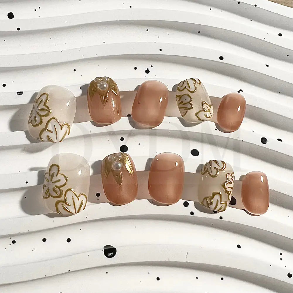 Golden Petals short round handmade press-on nails feature golden flower details and delicate pearl embellishment. 